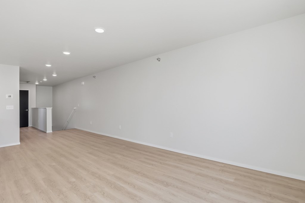 A large empty room with wooden flooring and white walls.