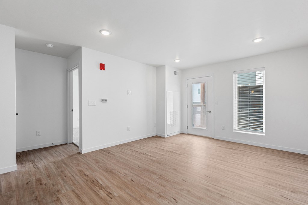 the living room of an apartment with white walls and wood floors