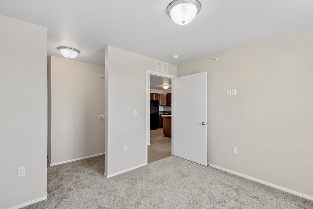 an empty living room with white walls and a door to a kitchen