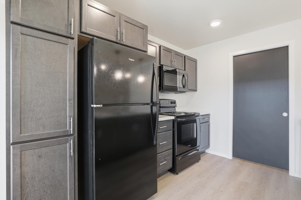 A black refrigerator is in a kitchen with wooden cabinets.