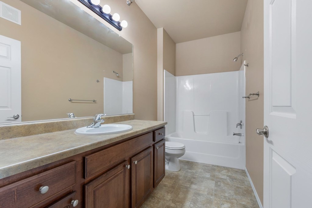 A bathroom with a sink, mirror, toilet, and bathtub.