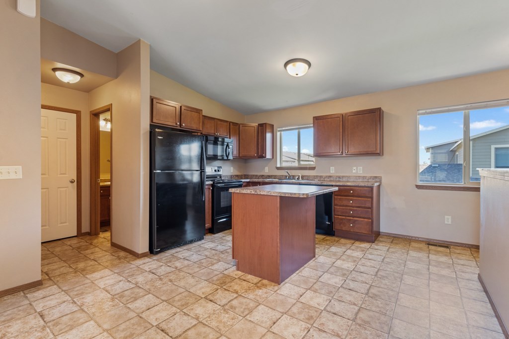 A kitchen with a black refrigerator and wooden cabinets.