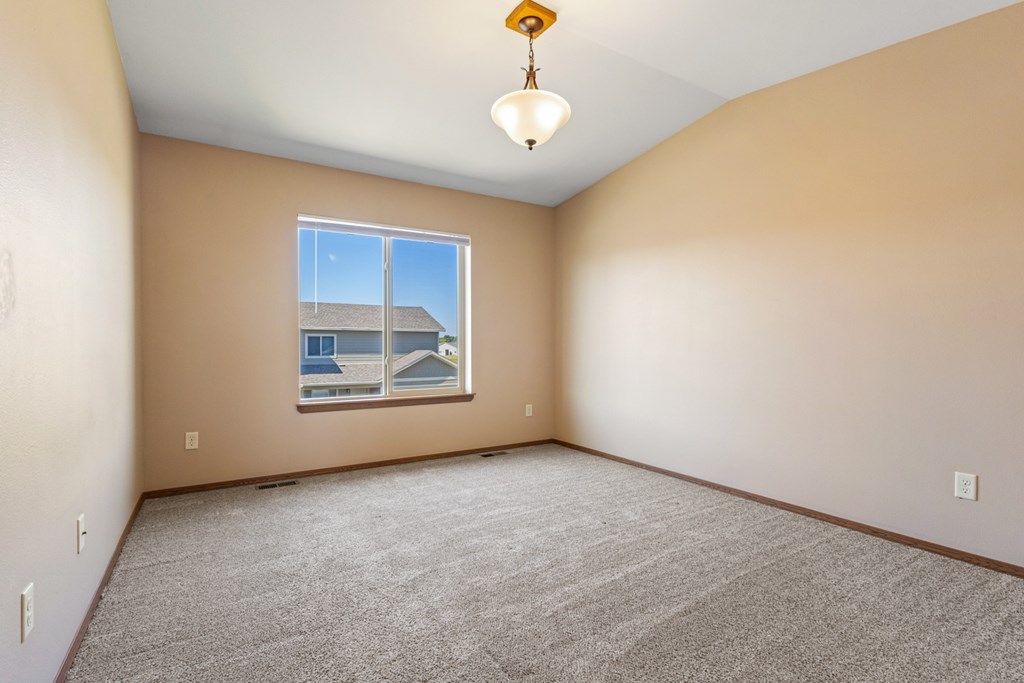 Empty room with a carpeted floor and a window showing a view of a house.