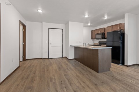 A kitchen with a black refrigerator and wooden floors.