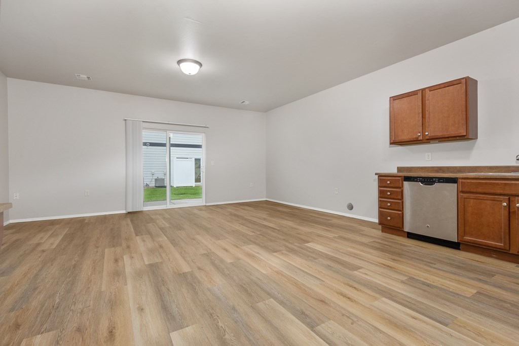 A room with wooden flooring and a window showing a view of a house.