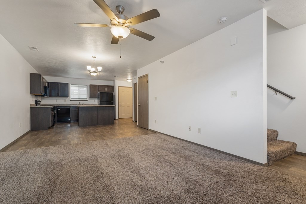 A spacious living room with a ceiling fan and a carpeted floor.