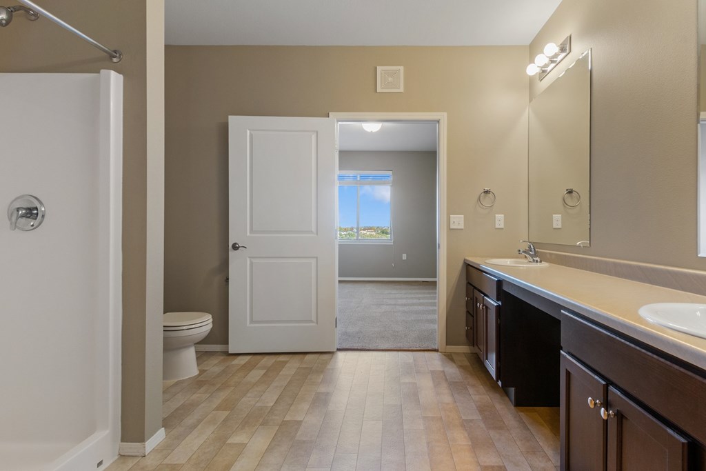 A bathroom with a white toilet, a white door, and a wooden floor.