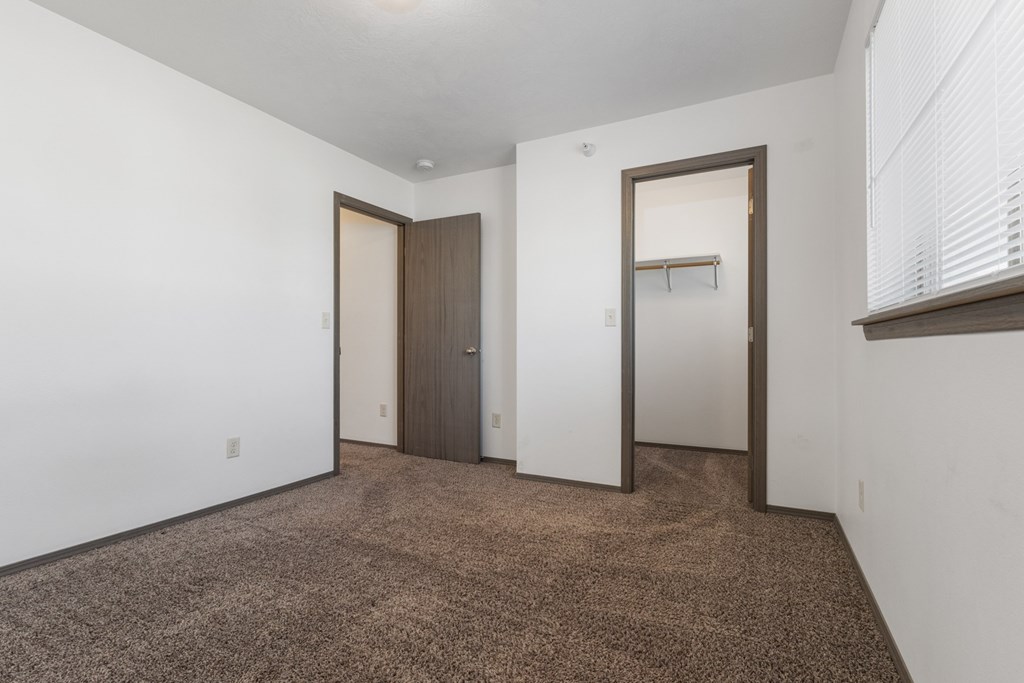 A room with brown carpet and white walls with two doors.
