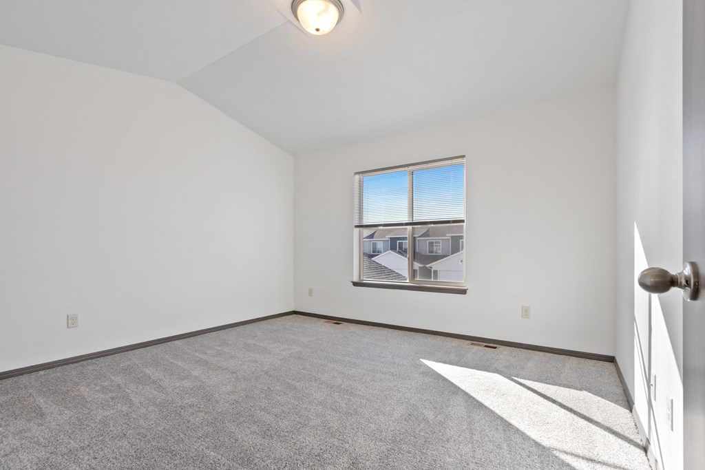 A room with a carpeted floor and a window showing a house view.