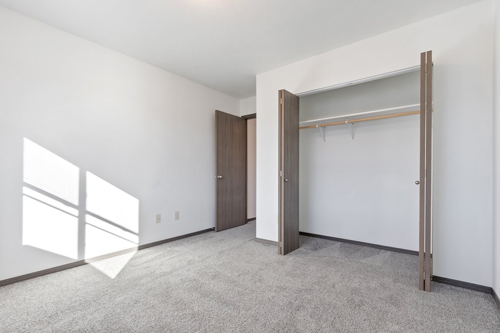 A room with a carpeted floor, a white wall, a wooden door, and a white closet with a metal rod.