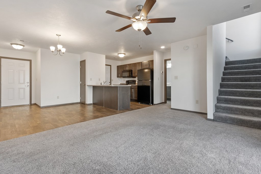 A living room with a grey carpet and a ceiling fan.