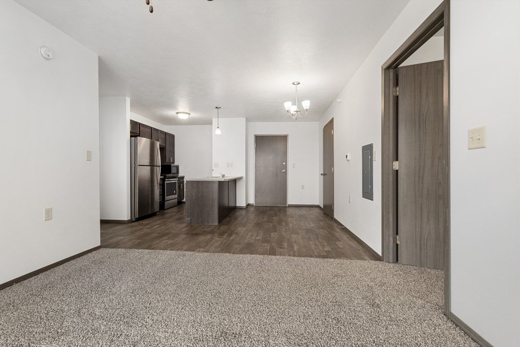 A spacious room with a carpeted floor and a kitchen area in the background.