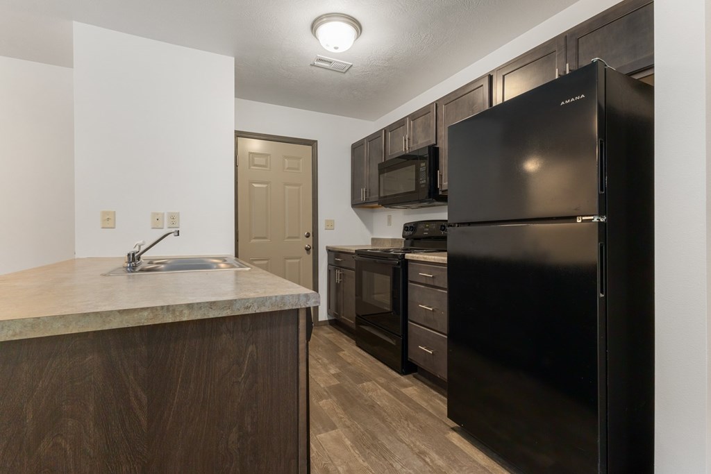 A kitchen with a black refrigerator and wooden cabinets.