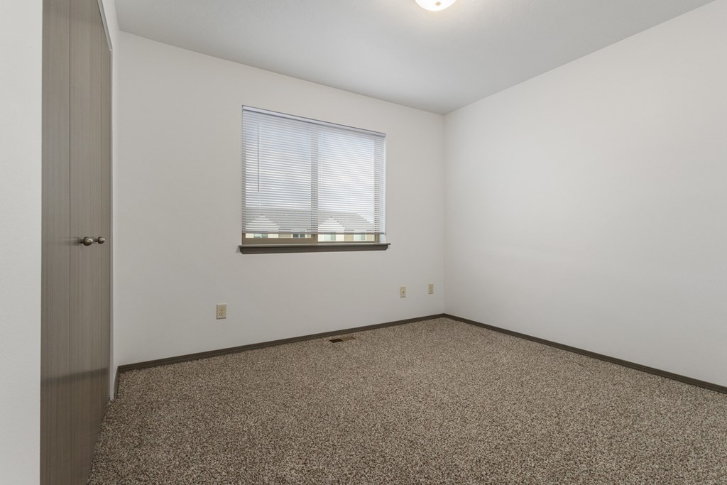 A room with a carpeted floor and a window with blinds.