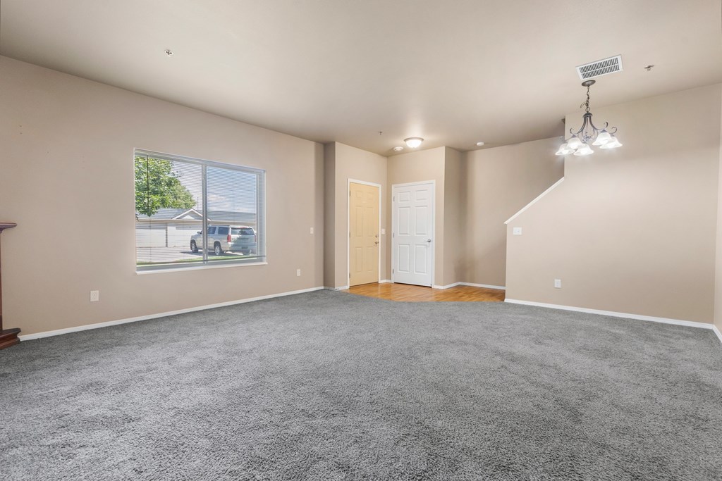A spacious room with a grey carpet and a large window.