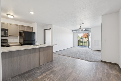 A kitchen with a black fridge and microwave, a wooden floor, and a door leading to a balcony.