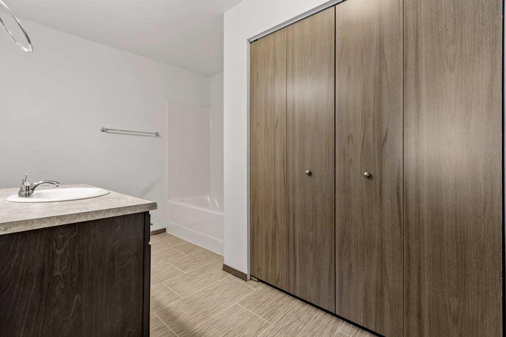 A bathroom with a sink, a shower, and a wooden cabinet.