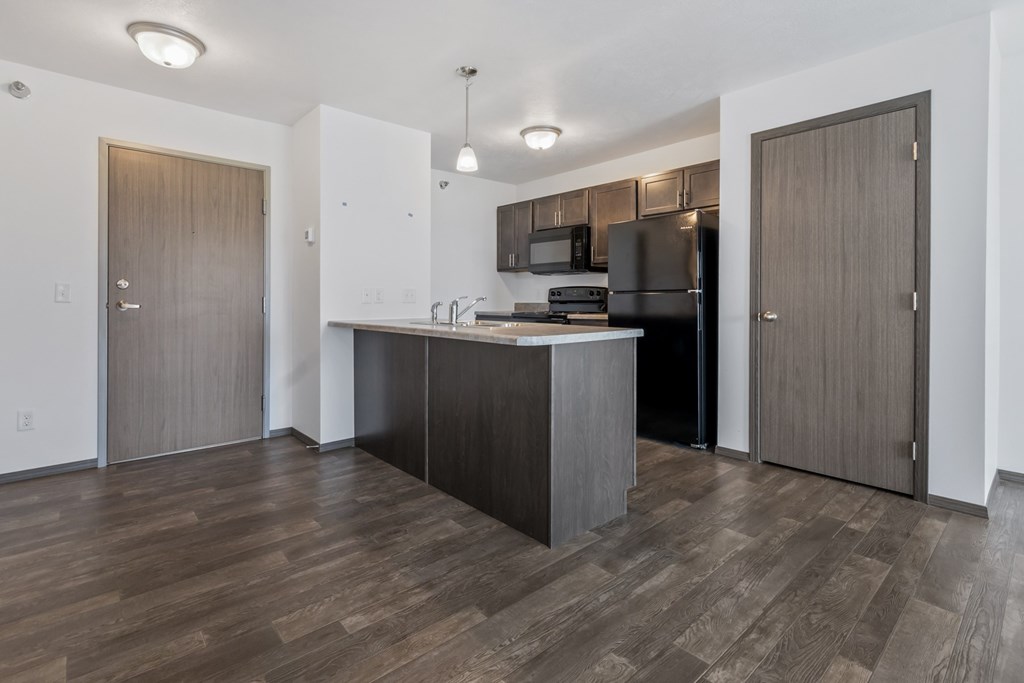 A kitchen with a black refrigerator and wooden floors.