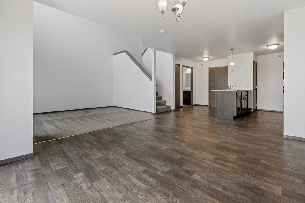 A spacious room with wooden flooring and a kitchen area in the background.