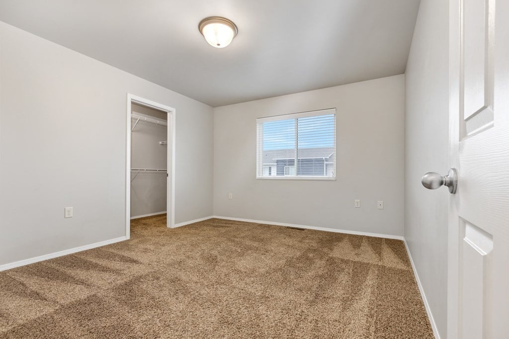 A room with a carpeted floor and a window with blinds.