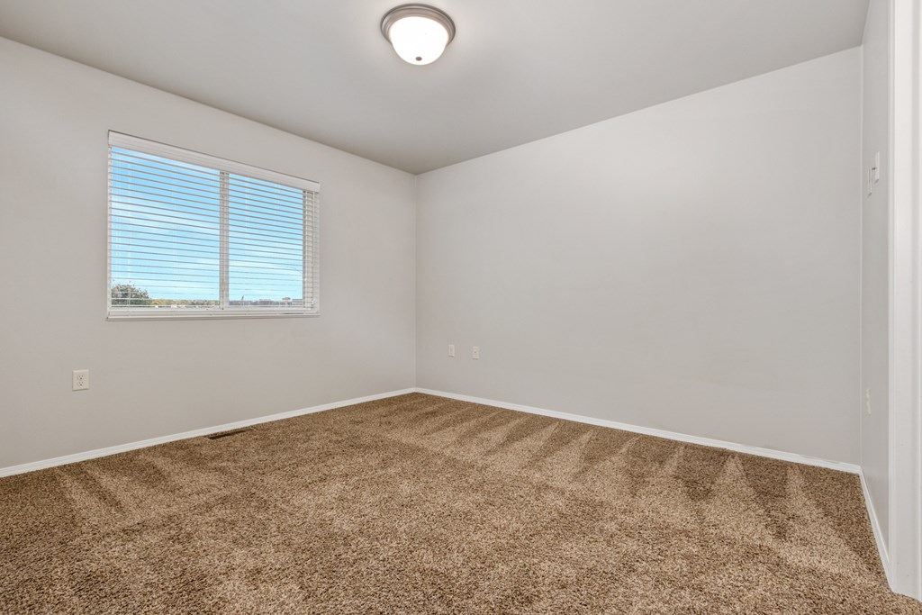 A room with a carpeted floor and a window with blinds.