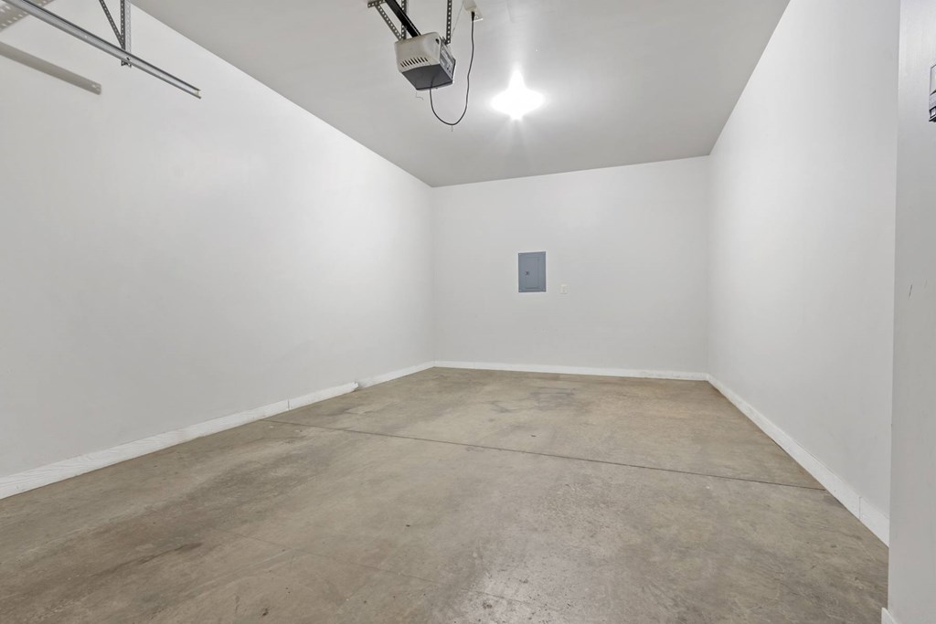 A room with a concrete floor and a white wall with a small square object on it.