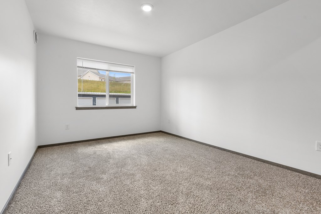 A room with a carpeted floor and a window showing a house and a fence outside.