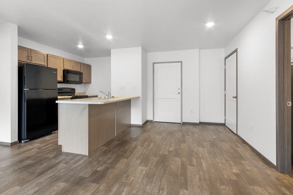 A kitchen with a black refrigerator and wooden floors.