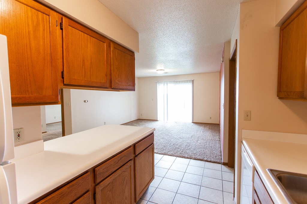 a kitchen with white countertops and wooden cabinets and a door to the living room
