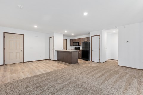 a living room with white walls and a kitchen with a black refrigerator