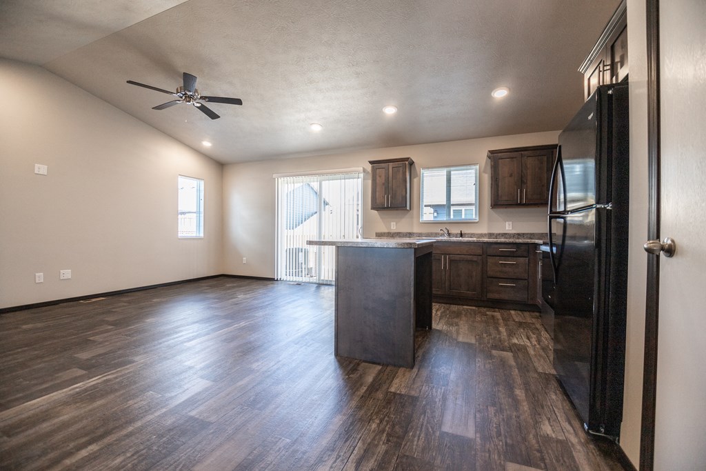 an empty living room with a kitchen and a ceiling fan