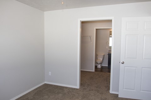 an empty bedroom with a door to a bathroom and a toilet