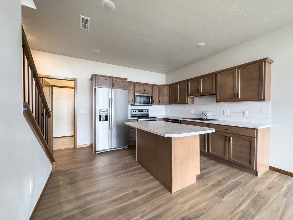 an empty kitchen with wooden floors and a stainless steel refrigerator