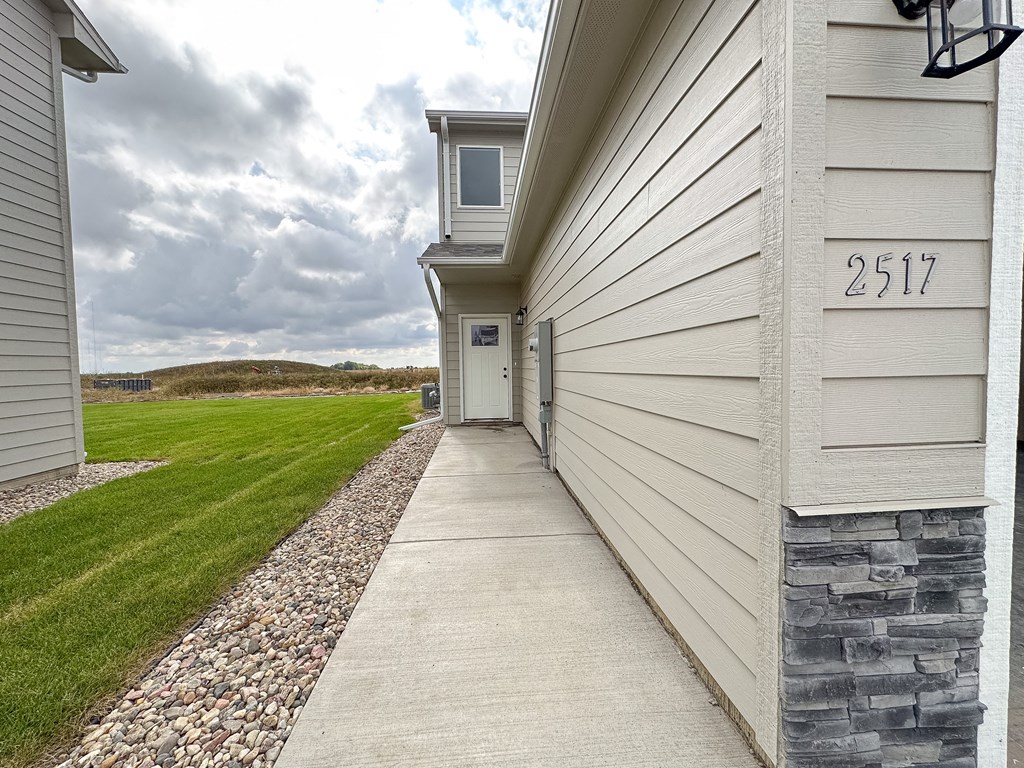 the walkway to the front door of a white house with a grassy field