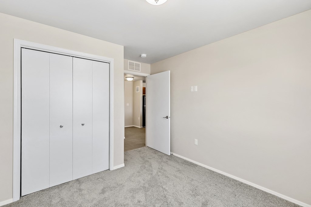 an empty bedroom with white closets and a carpeted floor