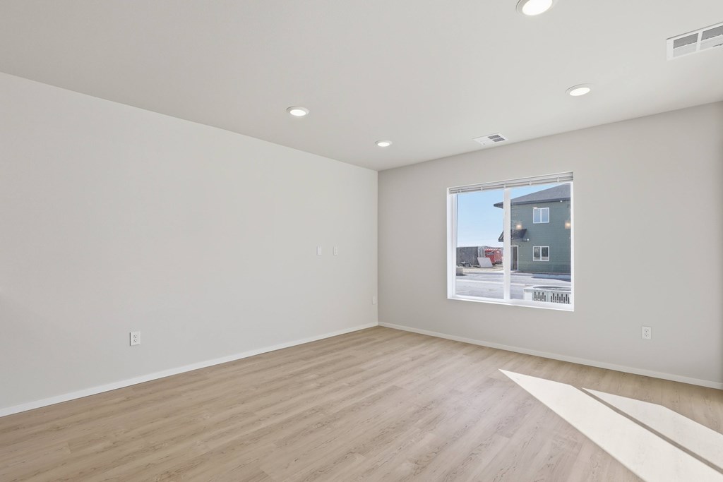 A large empty room with a window showing a house and a white floor.