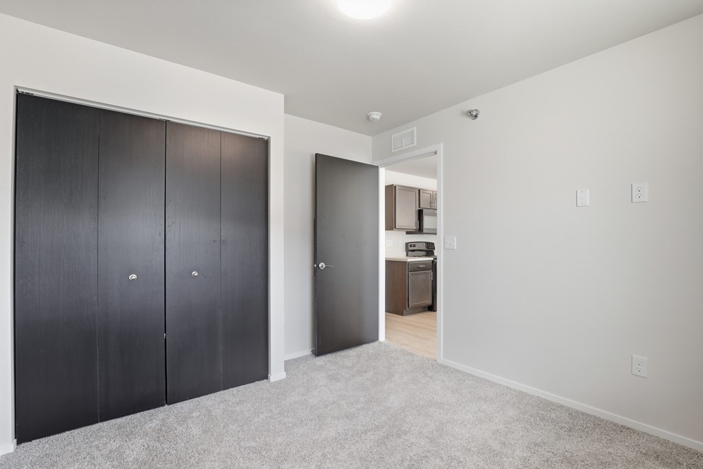 A room with a white wall and a carpeted floor with a black door on the left and a white door on the right.