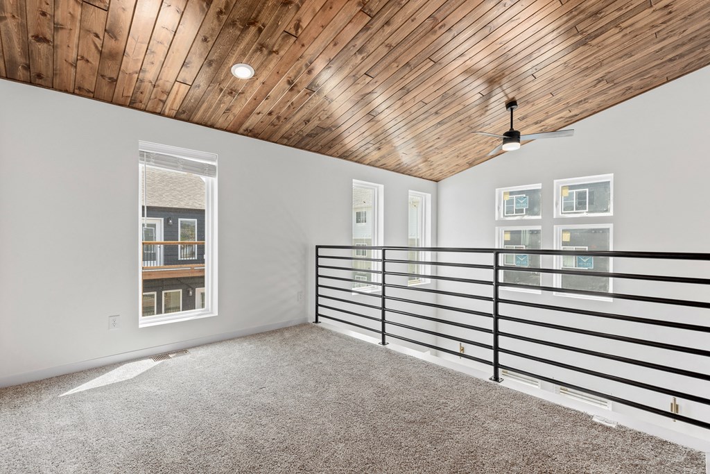 the upstairs loft has a wood ceiling and white walls and a balcony with railings
