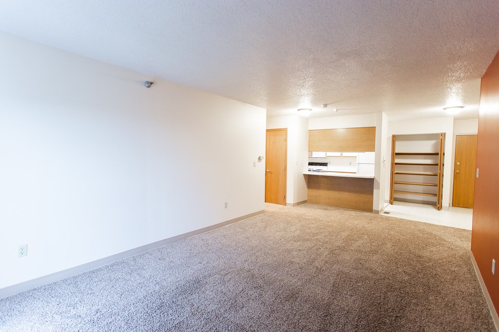 a empty living room with a white wall and a kitchen