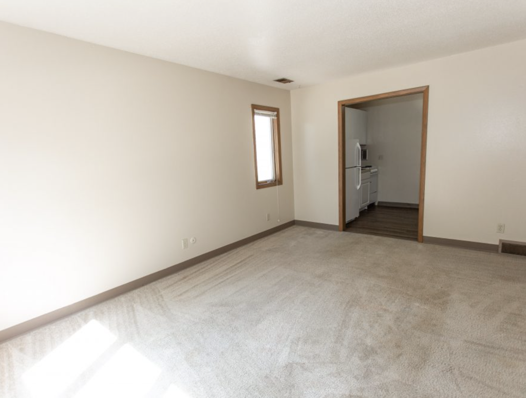 an empty living room with white walls and a door to a kitchen
