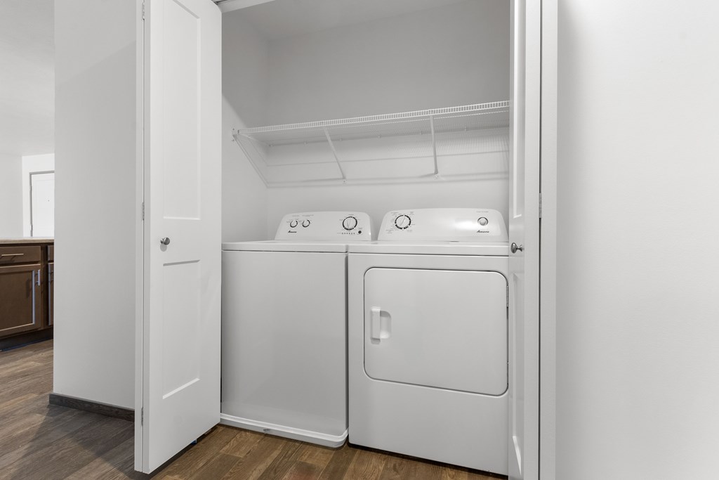 A white laundry machine is in a small, white closet.