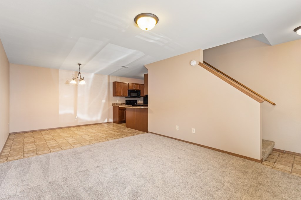 A spacious living room with a carpeted floor and a staircase on the right side.