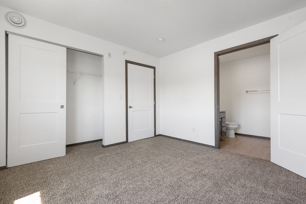 A room with white walls and a carpeted floor with four doors.