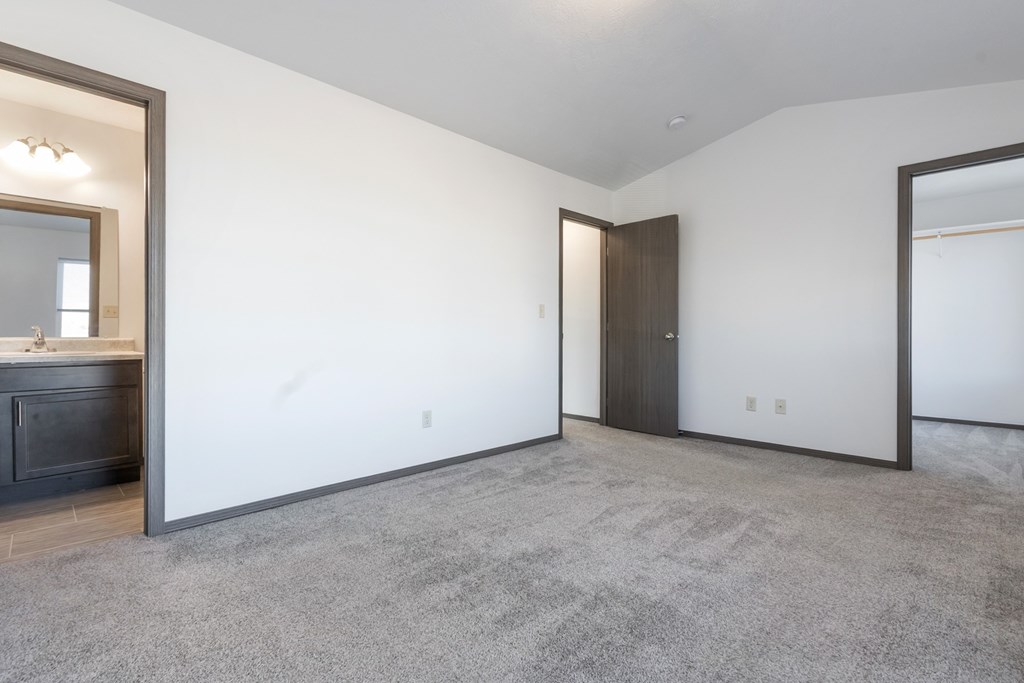 A spacious room with a grey carpet and a wooden door.