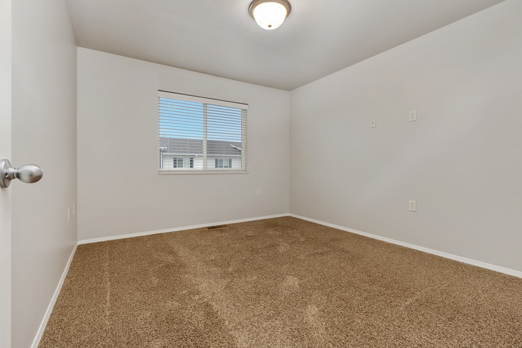 A room with a carpeted floor and a window with blinds.