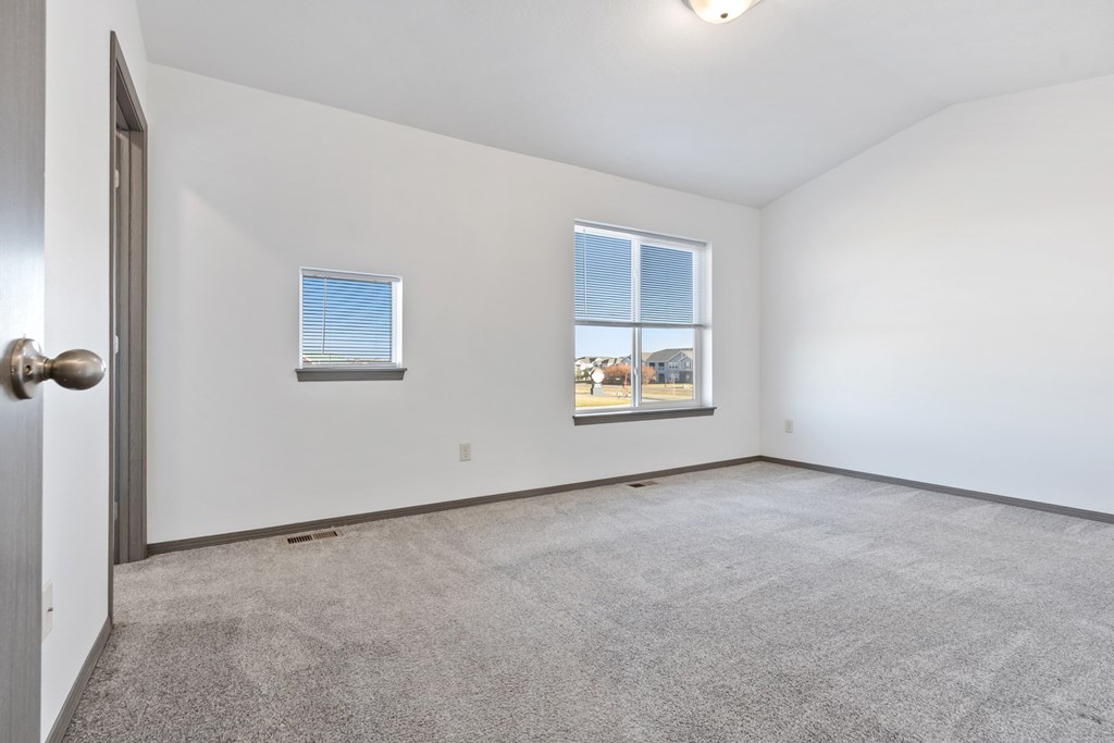 A room with a carpeted floor and two windows.