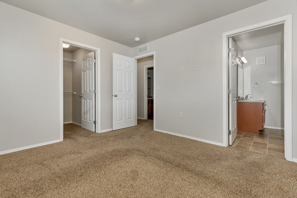 A room with carpeted floor and white walls with a doorway leading to another room.