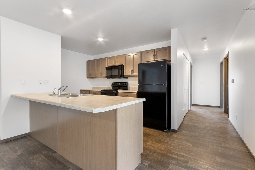 A kitchen with a black fridge and microwave, wooden cabinets, and a white countertop.