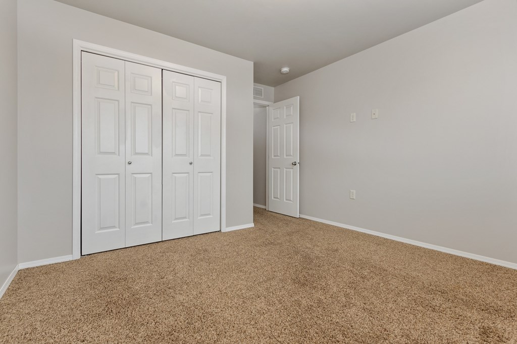 A room with carpeted floor and white walls with a white door and a white wardrobe with four doors.