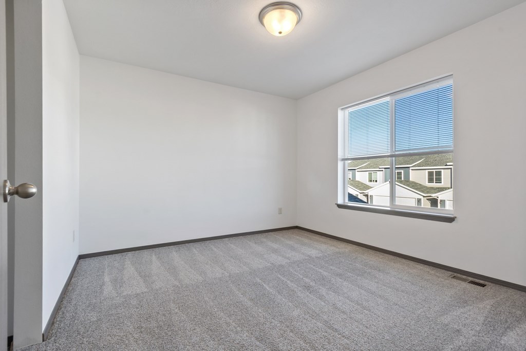 A room with a carpeted floor and a window showing a view of other buildings.